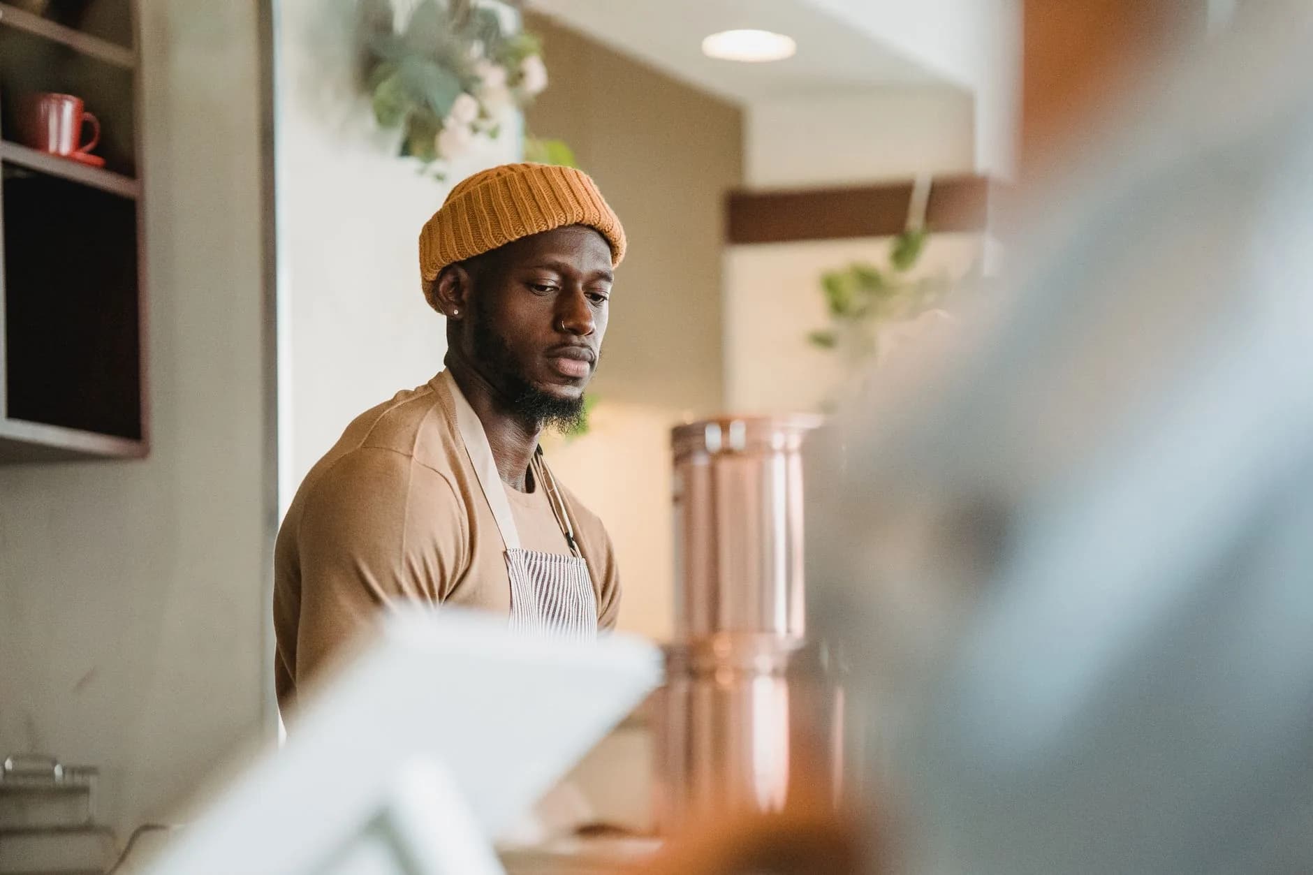 Barista in a mustard beanie and apron working behind a café counter